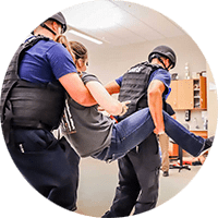 Active Shooter Response Training. Picture of two men carrying an injured woman across a room.